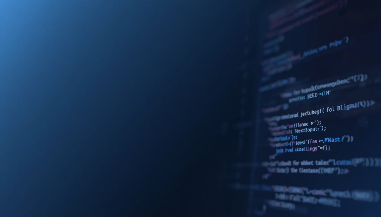 A close-up, shallow depth-of-field view of a dark computer screen displaying lines of code in blue, white, and pink text against a dark background.