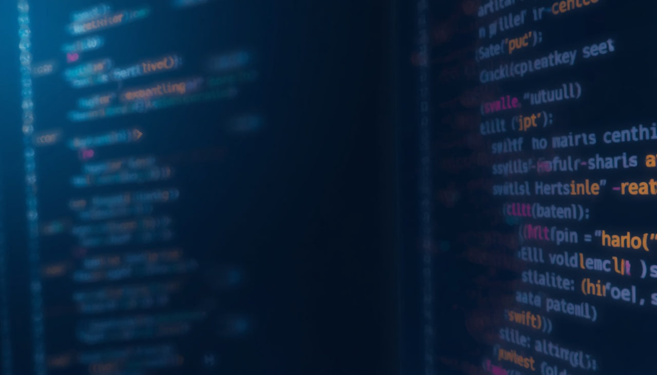 Close-up of a dark computer screen displaying lines of colorful programming code, with blue, pink, and orange syntax highlighted against a black background.